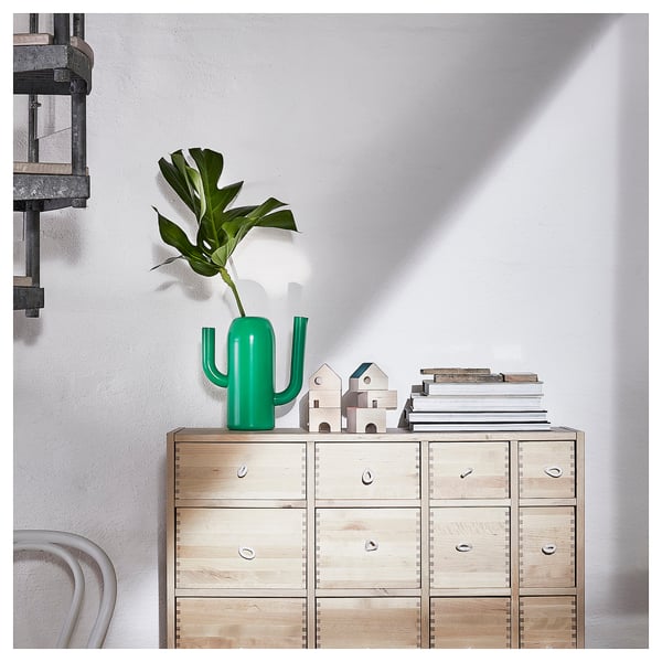 Bright green cactus-shaped vase on wooden dresser with sculptures and books.