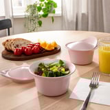 Pink bowls with salad, empty bowl, fruit, bread, oj, fork on napkin.
