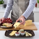 Person serving cheese on tray with crackers, jam, and grapes.