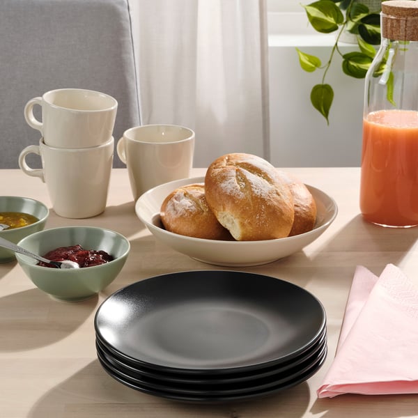 A breakfast table set with FÄRGKLAR side plates, mugs, bread, jam, juice, and napkins.