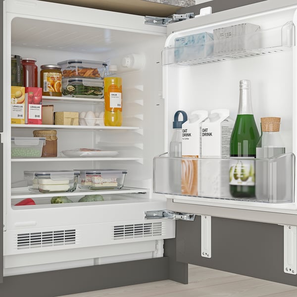 Open fridge with adjustable shelves, holding various foods and drinks, under cabinet.