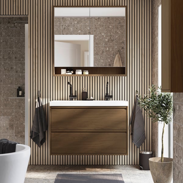 Modern bathroom with wooden vanity, mirror cabinet, and built-in lighting. Tall, sleek design fits between tiles, with plant and towels adding color.