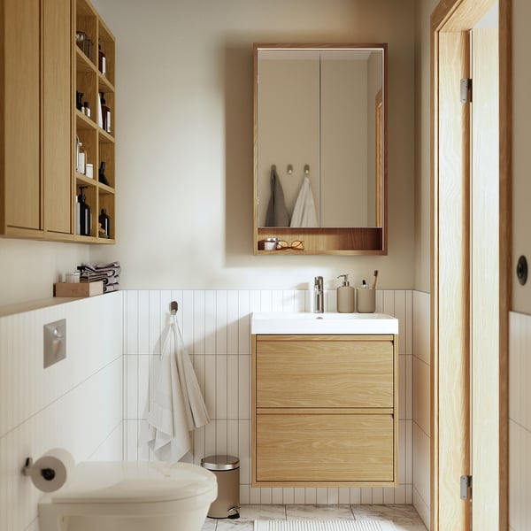 Modern bathroom with FAXÄLVEN mirror cabinet, sink, toilet, and cream tiling. Large mirror with lighting, hanging towel, and storage.