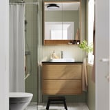 Wooden bathroom mirror cabinet with lights, above light wood vanity and frosted glass shower.