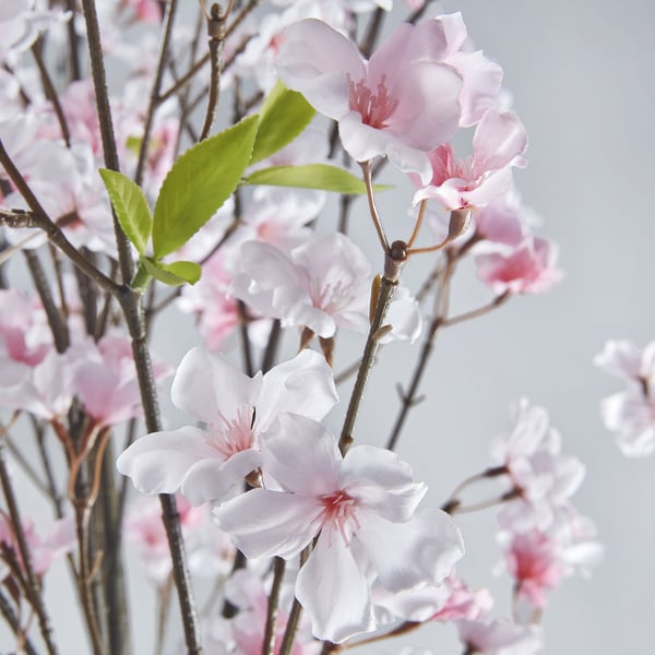 Artificial flowers in full bloom, featuring light pink petals and green leaves, arranged naturally on stems.