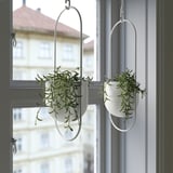 Two small FEJKA white pots hang from window, holding artificial green plants.