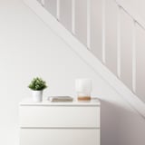 Minimalist room with white drawer, FEJKA plant, magazines, and lamp with cork base.