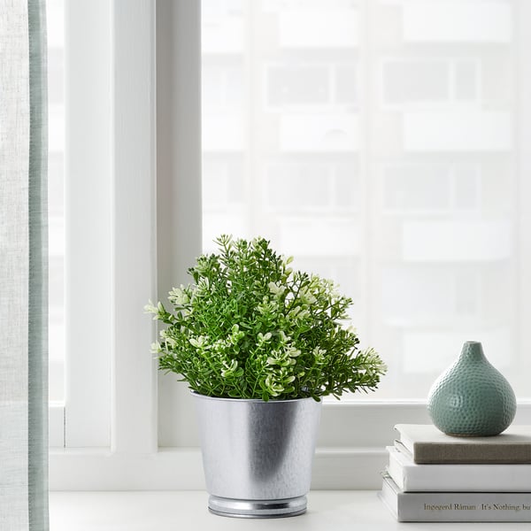 Artificial plant on window sill with books and vase.