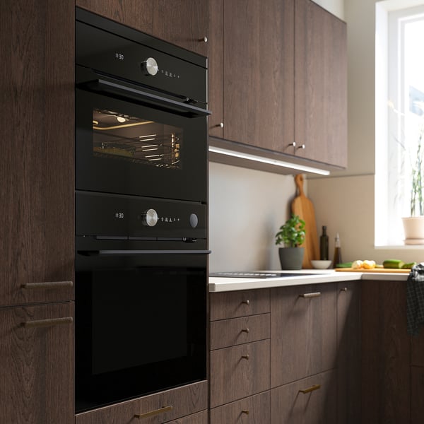 Modern kitchen black double oven built into dark wood cabinetry.