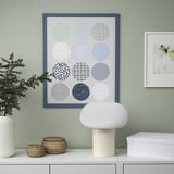 Colorful circle art print on green wall with lamp, basket, plant below; another print to right.