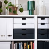 Modern bookshelf with FJÄDERHARV white & black files, green lamp, plants, and books. Files stand tall next to smaller items.