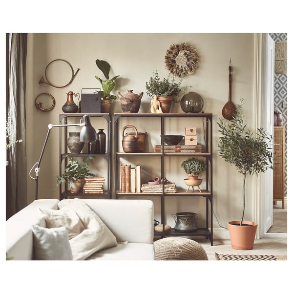 Modern living room with white couch, metal and wood shelving unit, potted plants, decorative vases, books, and wall hangings on beige walls.