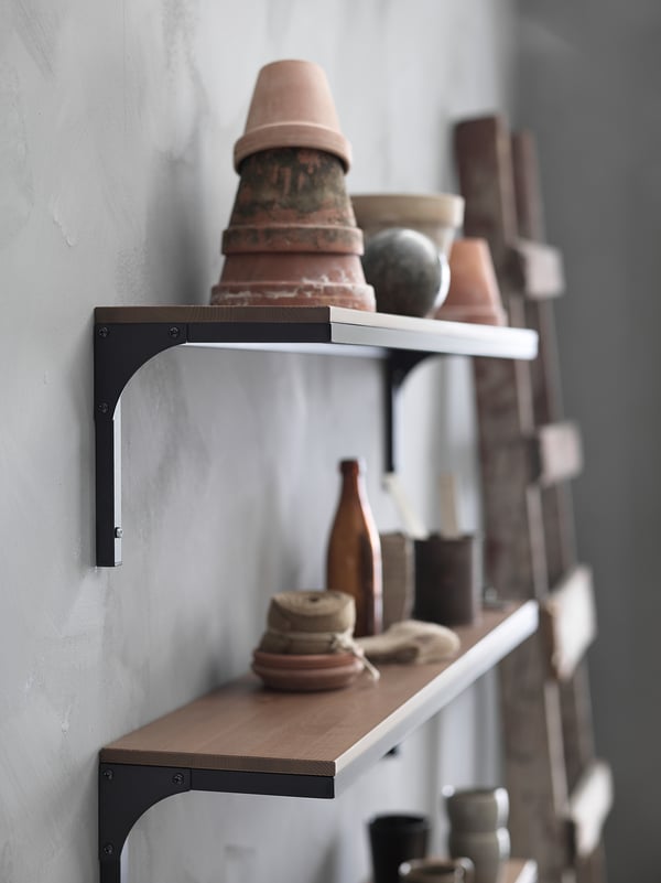 Industrial-style rustic wall shelf with metal brackets, holding assorted terracotta planters and vases.
