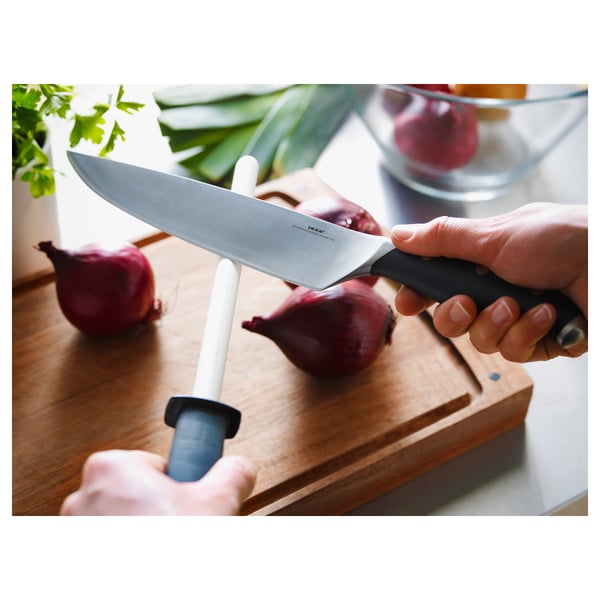 Person holding FLAKSA chefs knife, preparing to cut red onions on a wooden cutting board.