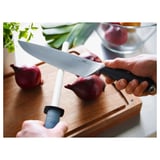 Person holding FLAKSA chefs knife, preparing to cut red onions on a wooden cutting board.