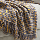Yellow & grey throw blanket with fringe, draped on beige couch