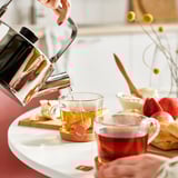 Pouring FLÖJT tea into clear cups with tea bags and pastries.