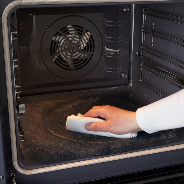 A person cleans an ovens self-cleaning feature, using a cloth. The oven has fan-forced air convection.