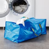 Large blue FRAKTA bag with yellow handles holds white towels near open washer.