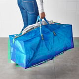 Person carrying a large blue ikea FRAKTA bag filled with laundry, by its sturdy handles.