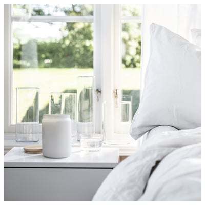 Clean bedroom by window, white candle, glass, wood coaster, clear glass cup on gray nightstand.