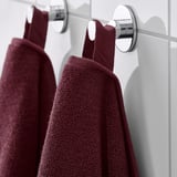 Two burgundy towels hang neatly on shiny metal hooks, showcasing their textured surface and cozy warmth.