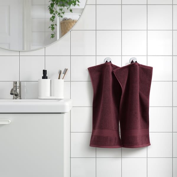 Plum towels on tiled wall, white sink, mirror, plants.