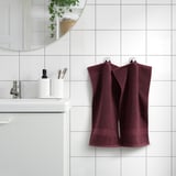 Plum towels on tiled wall, white sink, mirror, plants.