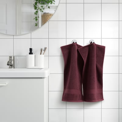 Plum towels on tiled wall, white sink, mirror, plants.
