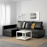 Modern minimalist living room with black FRIHETEN sectional sofa, colorful pillows, white coffee table, beige rug, floor lamp, and wall art.
