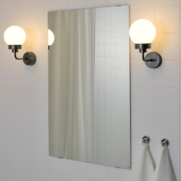 Bathroom with large mirror flanked by two lit wall sconces, reflecting glass globes and tiled wall. Two white towels hang on chrome hooks below.