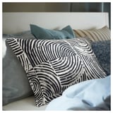 Bed with decorative pillows, one with black-white wavy pattern, others in stripes and solid colors.