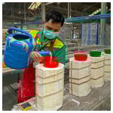Man in colorful shirt pours liquid into molds in workshop.