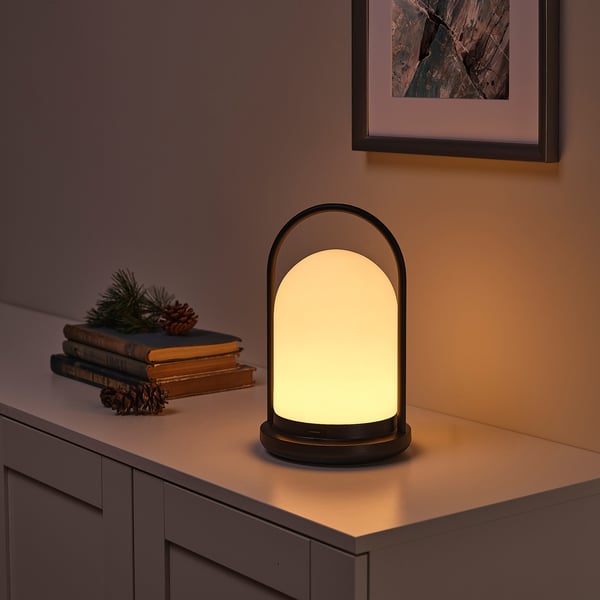 Modern lantern on a sideboard, casting warm, inviting light. Accompanied by books and pine cones, it adds a cozy ambiance.