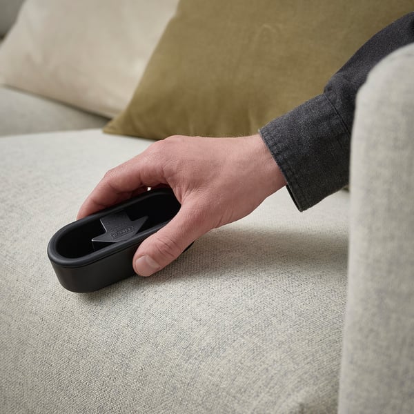 Persons hand holding a black reusable lint brush against a light-colored fabric.