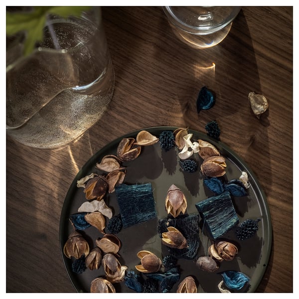 Dark green plate with dried brown plant pods and blue leaves. Two empty glasses on a wooden table.