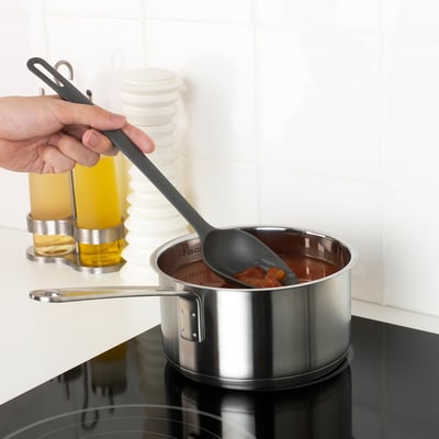 Hand stirring saucepan with gray spoon; capability of non-stick coating care.