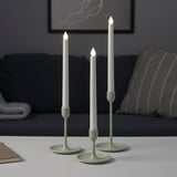 Threefigure of different height with lit candles on a table near couch.