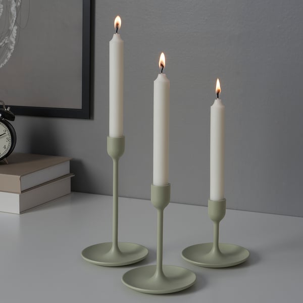 Three lit candles in green holders of varying heights on a table, creating a warm ambiance.