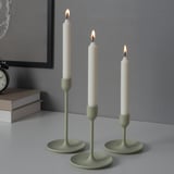 Three lit candles in green holders of varying heights on a table, creating a warm ambiance.