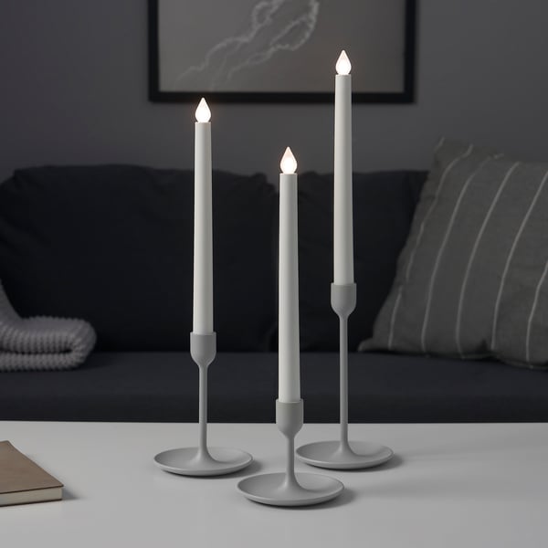Three modern silver candlesticks in varying heights on a table, providing atmospheric light.