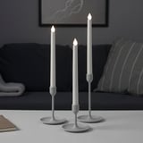 Three modern silver candlesticks in varying heights on a table, providing atmospheric light.