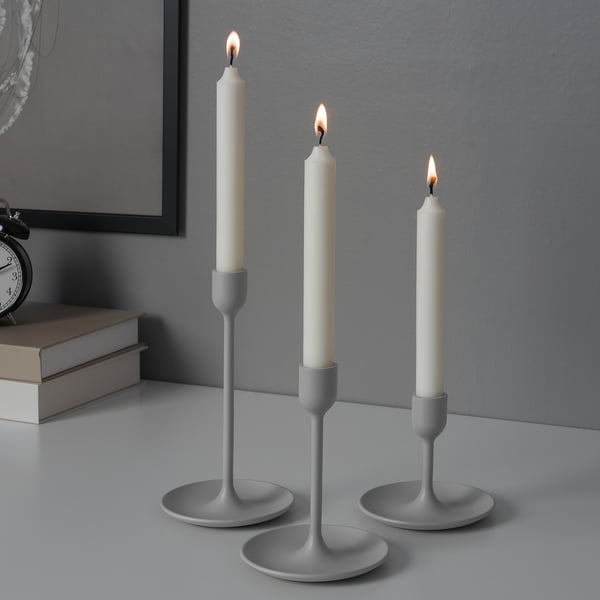 Three white candles in modern gray candlesticks, varying heights, lit on a table.