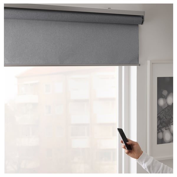 A hand holds a smartphone, controlling a modern blackout roller blind via IKEA home smart app, demonstrating smart control.