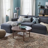 Large grey GADBJERG rug under a dark grey sectional, with a round coffee table and a large window.