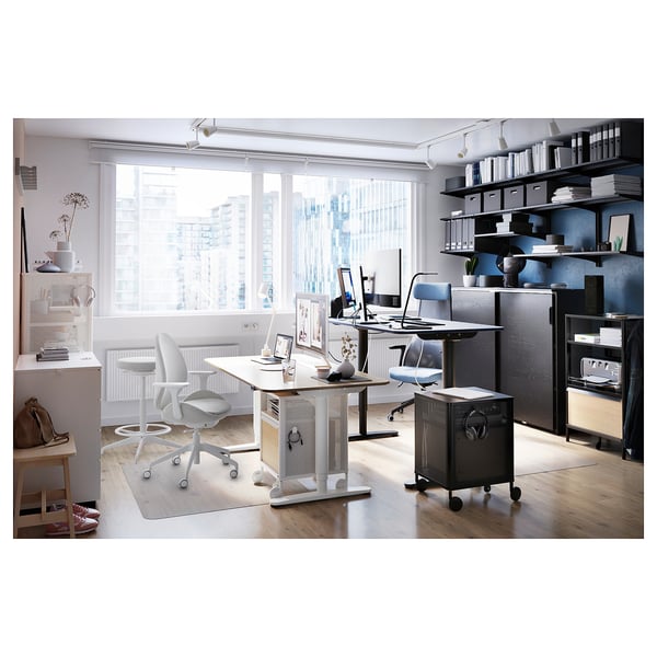 Modern home office with two desks, chairs, shelves filled with books and decor, and a large window offering a city view.