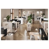 Modern office space with white furniture and plants, featuring desks, chairs, and storage units with sliding doors.