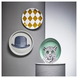 Three wall plates: harlequin pattern, top hat illustration, leopard design. Grey and mustard, white and black, and green background.