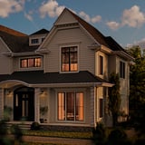 Modern house with GETKÅL multi-color lights; dark roof, light beige siding, greenery.