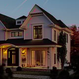 Decorated house with GETKÅL string lights. Grey house with lit windows, lit door, and string lights accenting the roofline, bush, and tree.